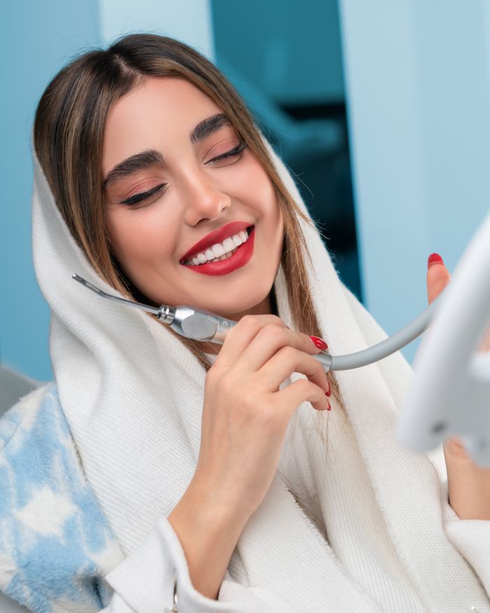 A young woman in a dental clinic smiling and holding a dental instrument, showcasing perfect dental health.